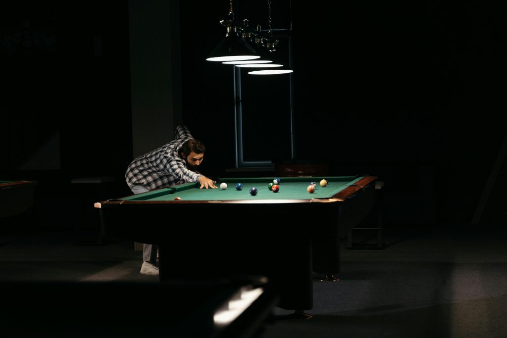 A focused man playing billiards on a pool table under dim lighting.